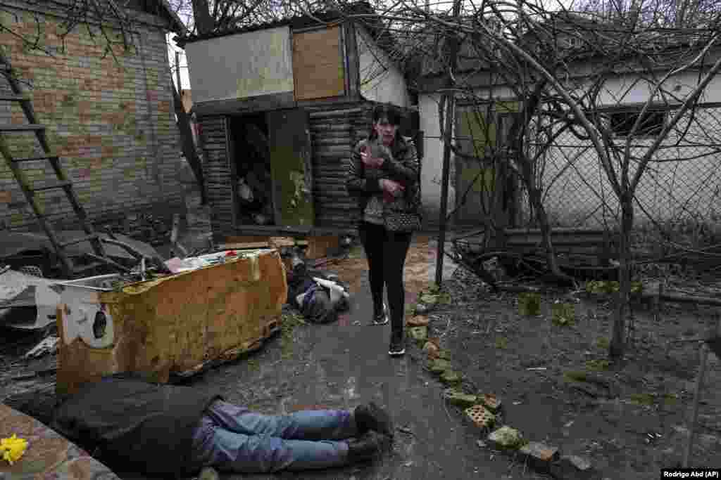 Ірина Гаврилюк з котом на руках проходить повз тіла свого чоловіка та брата. Буча, Фото від 4 квітня 2022 року. Українські слідчі встановили, що під час російської окупації Бучі загинули понад 1400 людей, із них 37 дітей