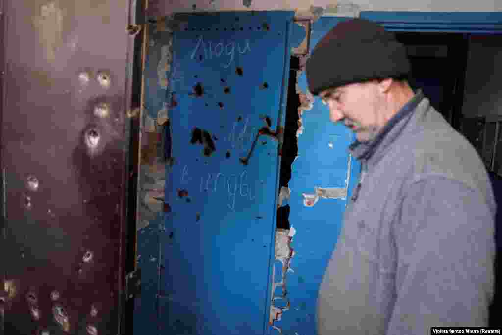Изрешечённые осколками снарядов двери в подвал. На дверях надпись, предупреждающая, что в подвале есть мирные люди. 56-летний Владимир слушает, как волонтёры пытаются убедить таких же мирных жителей, как он, покинуть Часов Яр 