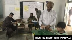 په پېښور کې یو کس خپل ماشوم د رایې ورکونې مرکز ته بیولی دی او ووټ اچوي - د اکتوبر ۱۶مې انځور.