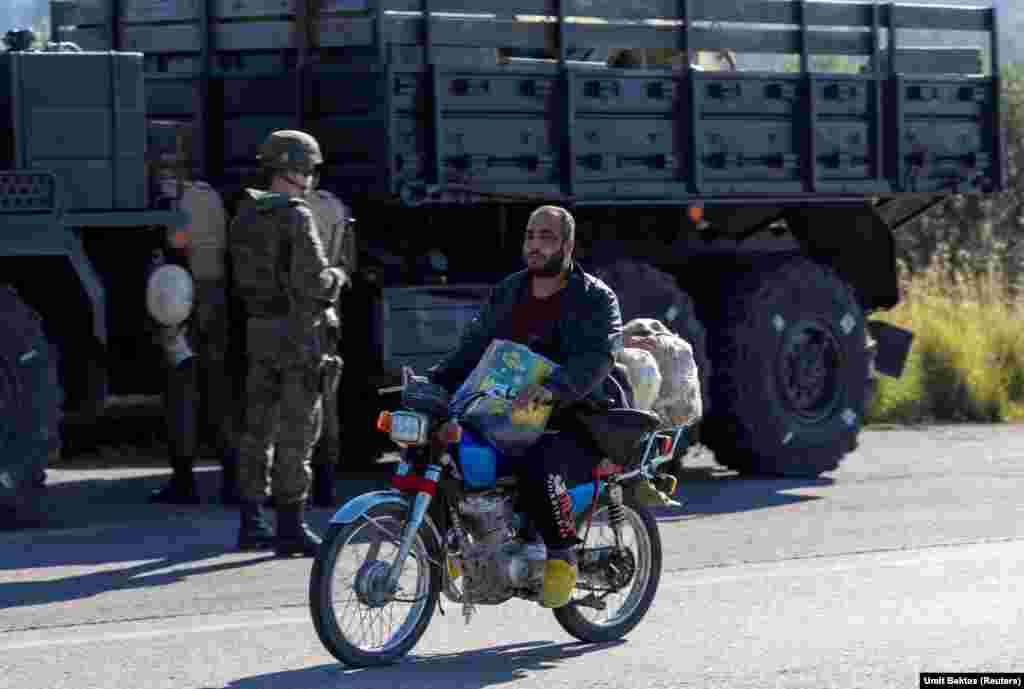 Un localnic trece pe lângă un convoi rusesc, în apropiere de baza aerienă Hmeimim. „Localnicii doar urmăresc ce se întâmplă”, spune fotograful turc despre situația din jurul bazei, care nu mai dispune de protecția militară externă oferită până recent de armata lui Assad. „În satul din apropierea bazei aeriene există o mulțime de magazine cu inscripții în rusă, dar toate sunt acum închise. Nu vezi soldați ruși care să iasă din bază singuri sau în mașini neblindate”, mai spune Umit Bektas.