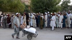 د شمالي وزیرستان یو وګړی په بنو کې د ملګرو ملتونو د خوړو ادارې ورکړې مرستې کور ته لېږدوي. ورسره، ګڼ کسان د مرستو ترلاسه کولو لپاره په قطار کې ولاړ دي - پخوانی انځور.