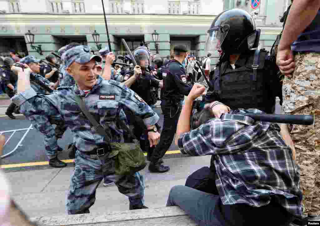 A Russian national guardsman beats a protester with a rubber baton during protests in Moscow. Video of the incident show the guardsman striking the detained man twice with full force, before a bystander punches the riot policeman on right. 