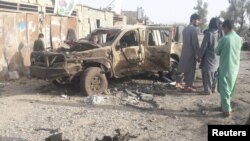 FILE: Residents look at an Army vehicle which was damaged during battle between Afghan security forces and Taliban in Farah Province in May.