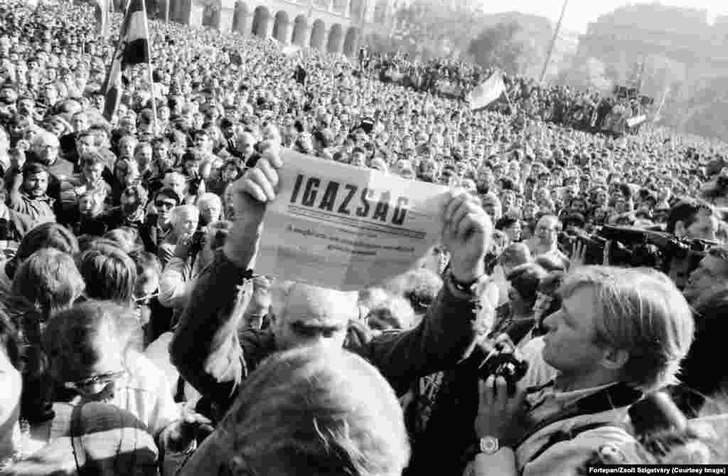Мужчина держит газету, на первой полосе которой написано, что Венгрия 23 октября 1989 года провозгласила себя демократической республикой. Заголовок объявляет этот день «давно назревшей, но ни в коем случае не запоздалой победой». Парламент Венгрии вскоре одобрил изменение Конституции страны. Поправки открыли возможности для свободных выборов. Исполняющий обязанности президента страны Матьяш Шурош объявил многотысячной толпе перед зданием парламента: «Я торжественно заявляю, что с сегодняшнего дня, 23 октября 1989 года, Венгрия является республикой и ее название — Венгерская Республика»