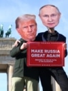 Участники акции протеста в Берлине в масках Дональда Трампа и Владимира Путина держат транспарант с лозунгом "Сделаем Россию снова великой"