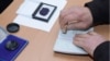 Armenia - An official at a polling station in Yerevan puts a special stamp on a voter's passport which is supposed to prevent multiple voting, 18Feb2013.