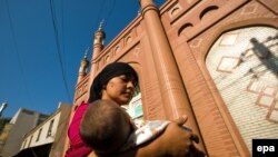 FILE: A young ethnic Uyghur woman carrying a baby walks in front of a mosque in Urumqi.