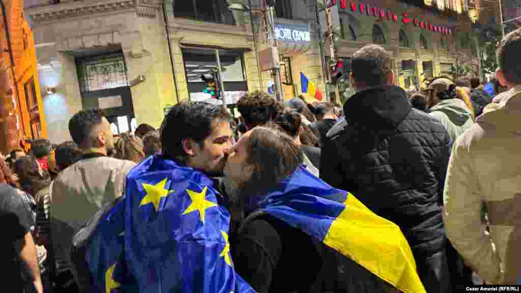 Doi tineri fericiți se sărută, după ce rezultatele exit-poll-urilor și rezultatele oficiale parțiale au indicat victoria democratului Nicușor Dan în alegerile prezidențiale din România, cu alte cuvinte menținerea direcției euroatlantice a țării. Mii de simpatizanții primarului Bucureștiului s-au adunat în fața clădirii istorice a Primăriei Capitalei, pe Bulevardul Elisabeta ca să celebreze victoria.