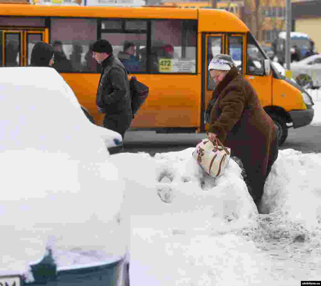У столиці тривають роботи із прибирання снігу на дорогах, тротуарах, зупинках. На фото: жінка проходить через купу снігу на узбіччі дороги, Київ, 11 січня 2016 року. 